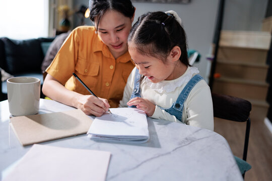 Woman helps daughter drawing in notebook.