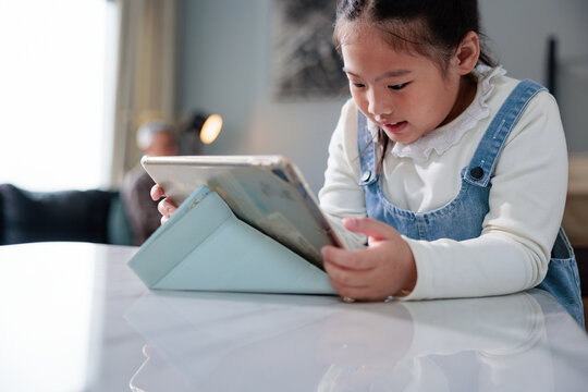 Girl intently using digital tablet on white table.