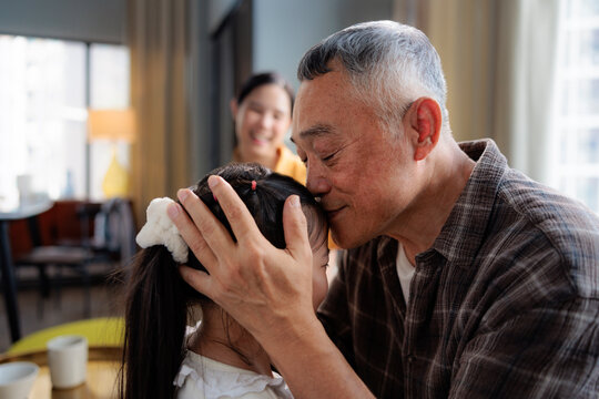 Grandfather lovingly kisses granddaughter, mother smiles
