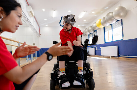 Young person in wheelchair interacting with therapist in gym