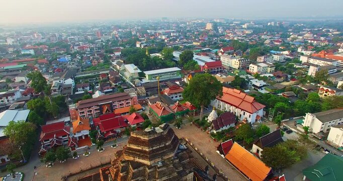 Aerial view of the iconic Chedi Luang temple complex at sunrise in Chiang Mai. Golden light highlights the ancient pagoda, detailed stucco design, and naga serpent sculptures lining the stairway