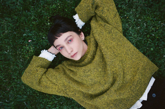 Young female lies on green grass wearing a loose sweater