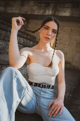Fototapeta premium Sensual close up portrait of attractive young woman posing on stone stairs while playing with her braided hair