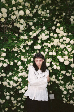 Young person stands in front of white flower wall with arms crossed