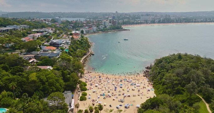 Shelly Beach in Sydney, people relaxing and enjoying the summer sun and clear ocean waters. Surrounded by green coastal trees park and residential buildings. Travel Australia. Aerial view drone flight