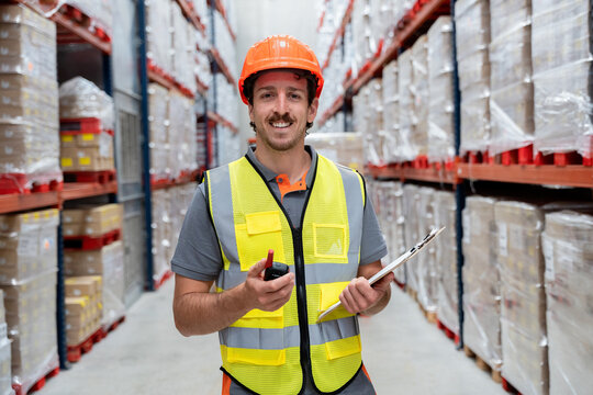 Warehouse worker smiling wearing safety vest helmet checking inventory