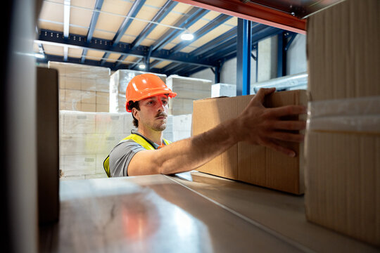 Warehouse worker organizing cardboard boxes on storage shelf