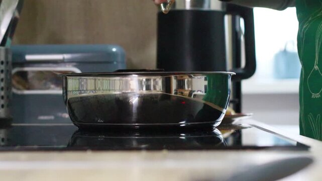 close-up of hands cracking a fresh egg into a frying pan while preparing a sunny side up egg. The eggshell is placed on the kitchen countertop after cracking. Concept of home cooking, breakfast prepar