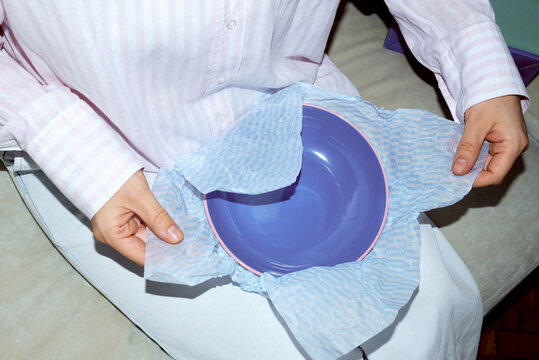 Woman unwraps a bowl from blue tissue paper while sitting on a sofa 