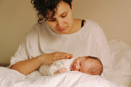 Close-up of caring mother gently stroking her sleeping newborns back 