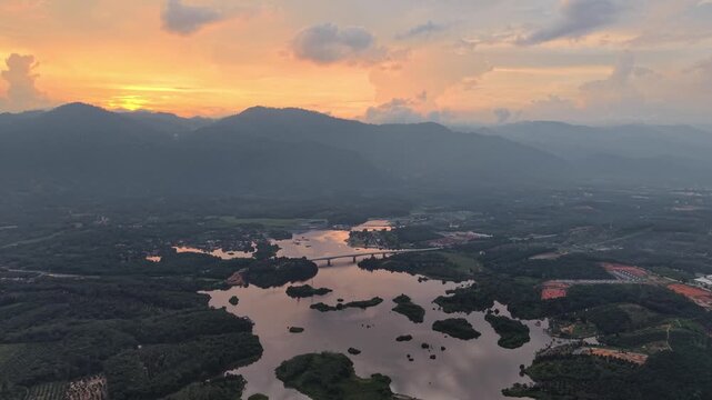 Aerial shot of a river winding through forested mountain landscape under colorful sunset sky with scattered clouds, showcasing peaceful natural beauty at Tasik Raban