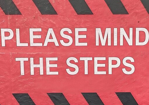 Please Mind the Steps Safety Warning Sign on Red Textured Concrete Surface