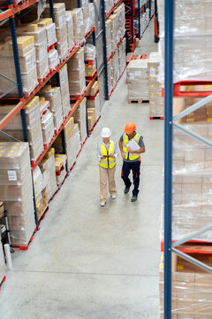 Logistics workers walking through large warehouse aisle