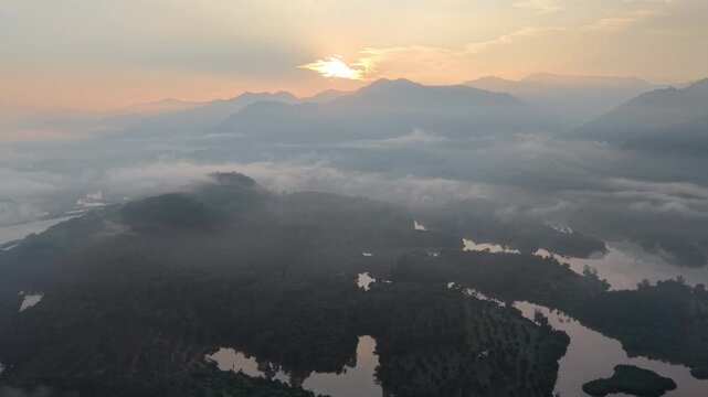 A serene misty mountain landscape at sunrise featuring dense forest, calm water bodies at Tasik Raban
