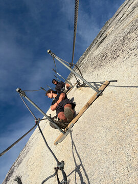 Two young men sit on face of Half Dome, in the cables