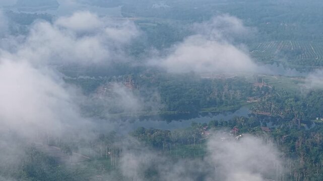 A serene aerial view showing a mist covered landscape with forest, a lake, and scattered houses in a rural countryside during a foggy morning at Tasik Raban