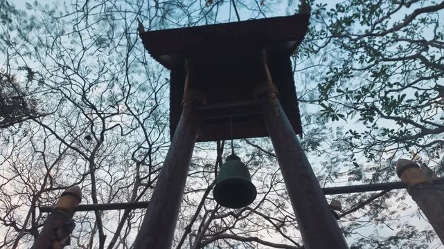 Buddhist temple bell hanging in wooden structure Thailand, Sacred metal bell in tropical temple garden with spiritual atmosphere 4k