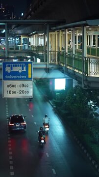 Bangkok night traffic on Sukhumvit road with pedestrian overpass and moving vehicles, Urban city street with neon lights reflections and transport motion in Thailand, 4k vertical video