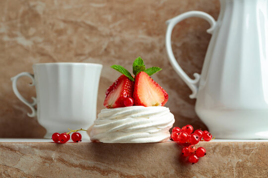 Pavlova dessert with strawberries, red currant, and mint on a beige table.