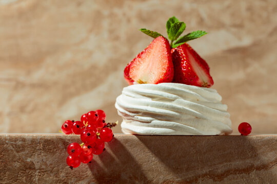 Pavlova dessert with strawberries, red currant, and mint on a beige table.