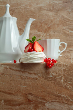 Pavlova dessert with strawberries, red currant, and mint on a beige table.