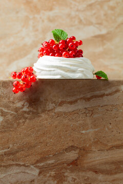 Pavlova dessert with red currant and mint on a beige table.