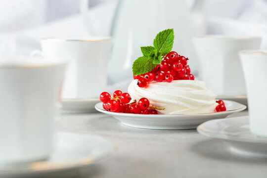 Pavlova dessert with red currant, and mint on a white table.