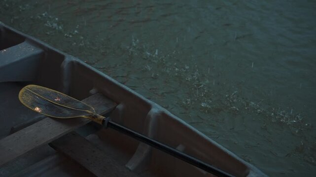 Small boat with paddle during rainfall on canal water, Raindrops splashing around rowing boat with wooden seat and paddle on water surface 4k