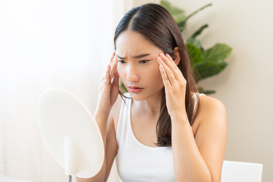 Anti aging, worry puberty asian young woman, stressed girl looking in mirror, allergy presenting an allergic reaction from cosmetic on face. Beauty, health care from acne problem, dry skin, treatment.