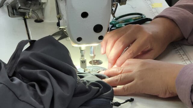 Close up of a worker's hands sewing black fabric with an industrial sewing machine in a garment factory