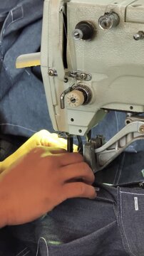 Close up of worker hands operating industrial buttonhole sewing machine on denim jeans, vertical video