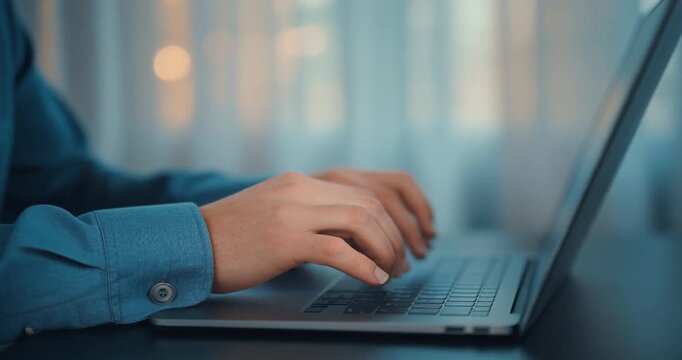 Man in Blue Shirt Typing on Laptop Keyboard in Soft Evening Light
