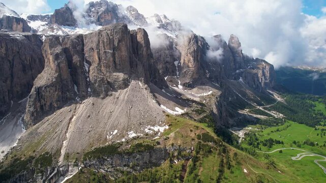 Passo Gardena Dolomites Italy 4K Drone. Aerial flight along peaks at cloud level Green valley landscape below majestic rocky cliffs overflight scenic cinematic travel b roll stock video asset