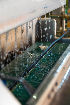 Industrial Metal Finishing: A close-up view of a metal object undergoing a finishing process in an industrial setting, immersed in a vat of green liquid, with water dripping from above.