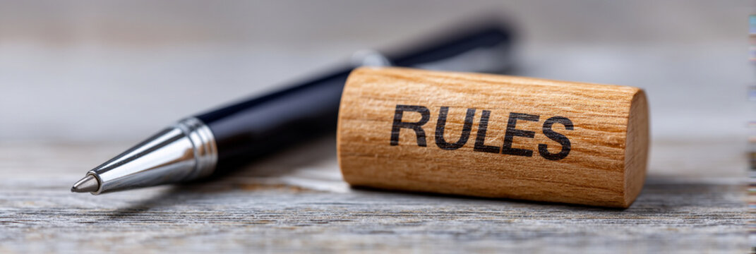 Wooden block with "RULES" engraved, resting on dark surface. Image conveys authority, discipline, or structure. Useful for workplace, school, or organizational themes