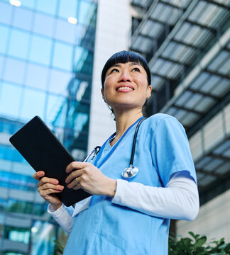 Portrait of an asian female woman doctor or nurse and  caretaker health care worker holding  a tablet computer in front of hospital or clinic or nursing home outside