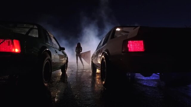 Street racing scene at night with a woman holding a checkered flag between two muscle cars