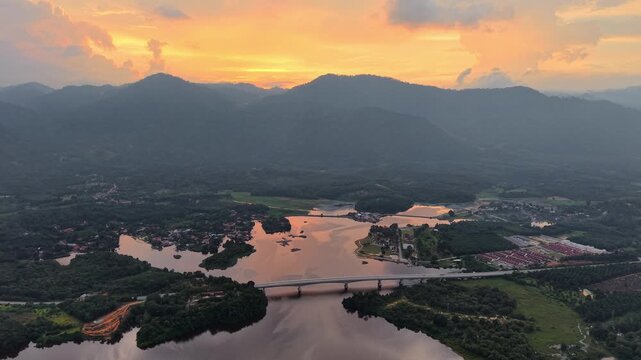Sunset colors paint the sky in warm oranges. Mountain peaks glow softly in the distance at Tasik Raban