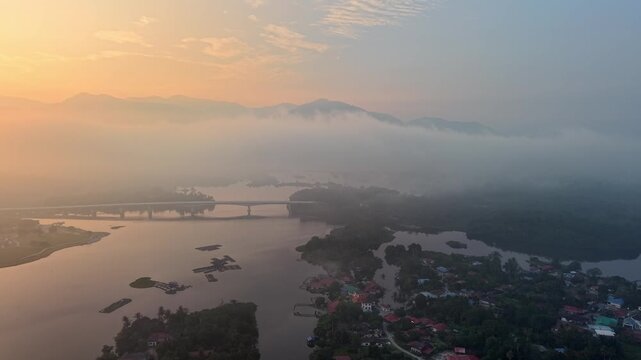 Aerial view of a small town near a river at early morning with mist covering hills and calm water at Tasik Raban