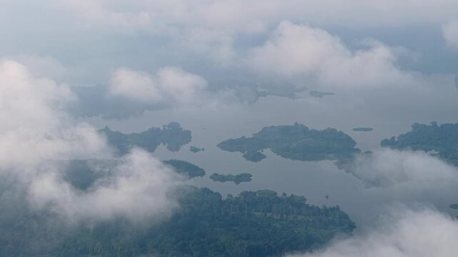 Aerial shot shows clouds moving over distant islands. Water reflects soft light in misty landscape at Tasik Raban