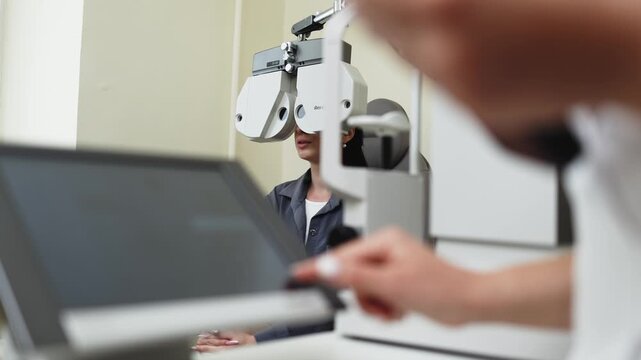 Young woman receiving a comprehensive eye examination with a phoropter in a modern eye clinic. Concept vision care, ophthalmology, eye diagnostics, preventive medicine, healthcare.