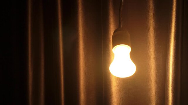 Glowing Light Bulb Hanging Against Brown Curtain