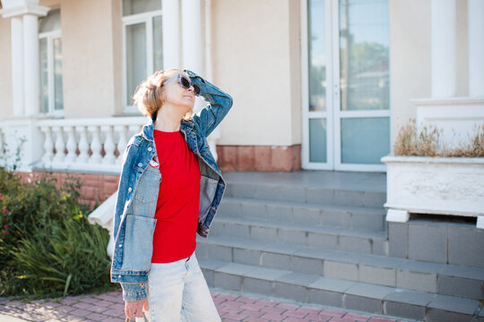 Stylish senior woman 50-55 year old wearing denim jacket and eye glasses walking in city street.
