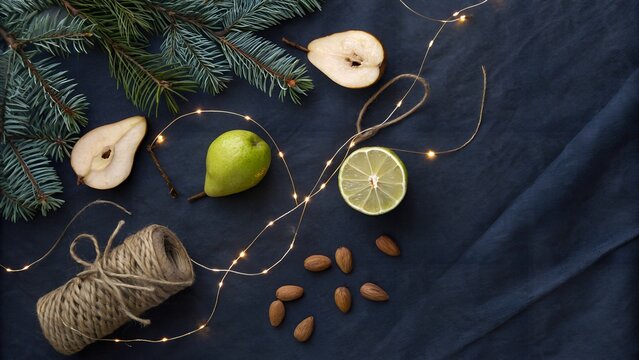Flat lay of pear slices, lime, almonds, and pine branches on a dark blue fabric background
