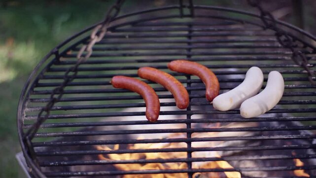 Grilled sausages and white sausages cooking on a round swinging grill grate over an open fire