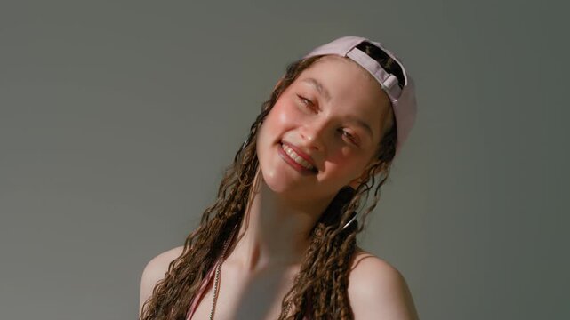 Woman posing with expressive face, backward cap, hoop earrings and braided curls on gray background