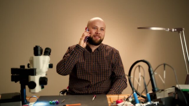 Repair technician taking a phone call at an electronics workbench with microscope and tools