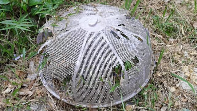 Broken and weathered plastic food cover dome discarded on the grass, showing environmental pollution and plastic waste.
