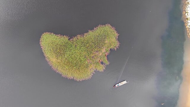 Aerial view of a heart shaped island in a calm lake. Dark water surrounds the green landmass at Tasik Raban