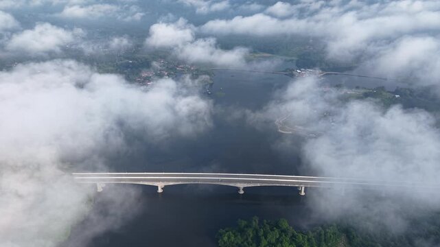 Aerial view shows a bridge piercing through thick clouds. Below. The bridge spans the water at Tasik Raban